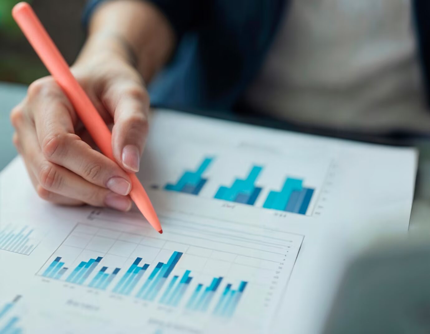 Person marking blue bar graphs with orange pen during data analysis or report review.